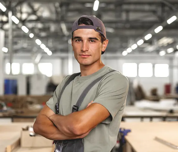 Un jeune artisan, bras croisés, dans un atelier de menuiserie